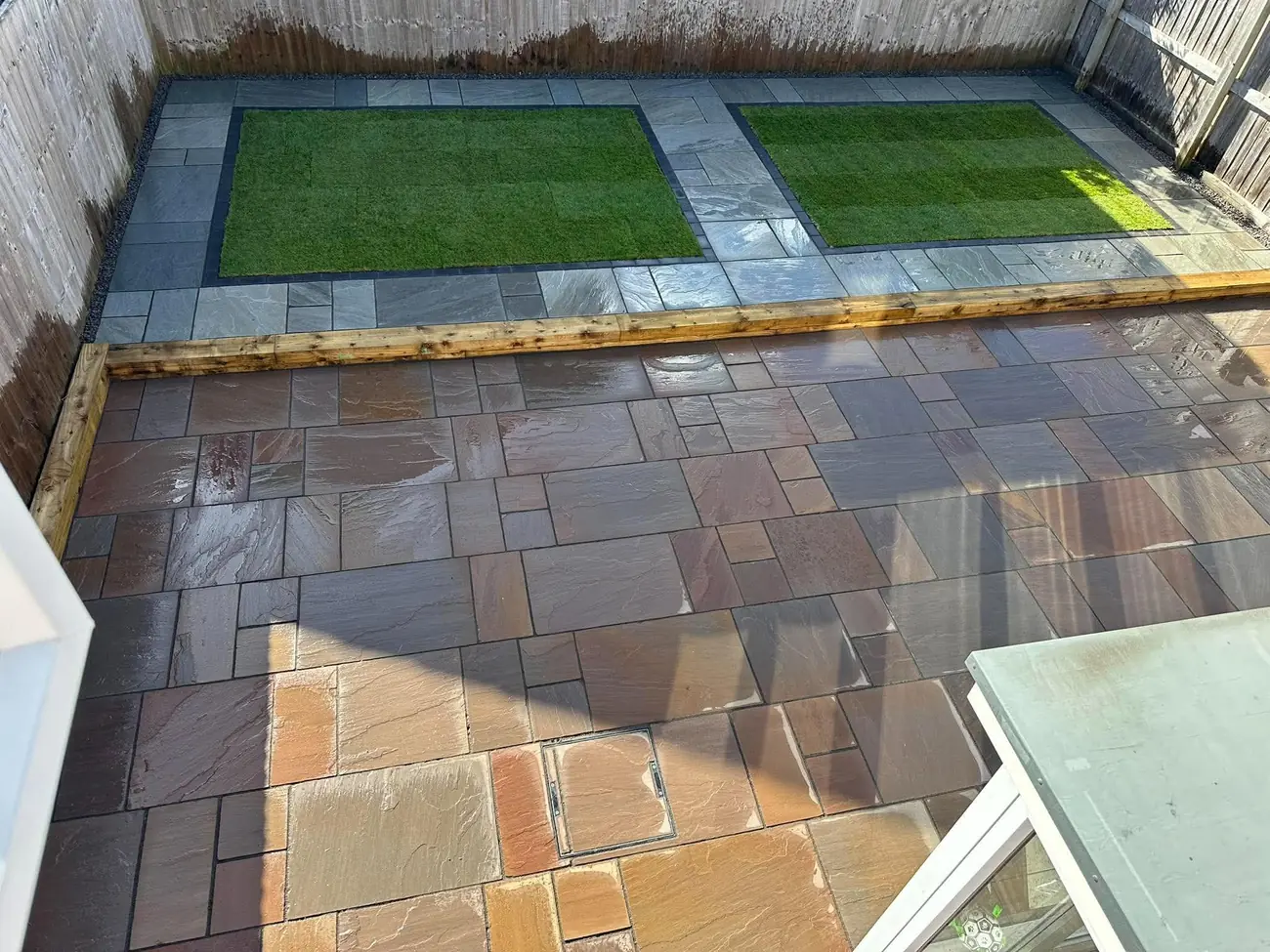 Indian stone patio with two artificial grass panels framed by block edging