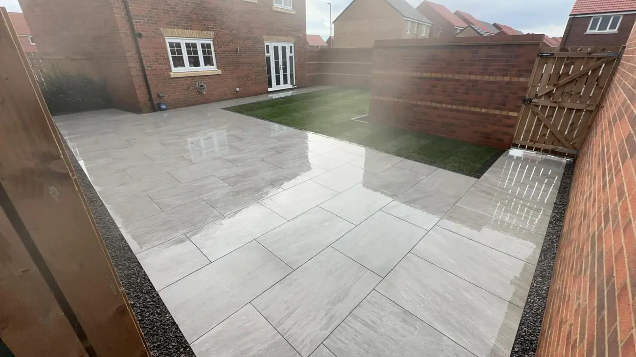 Glossy porcelain patio and turf lawn beside a brick wall and gate