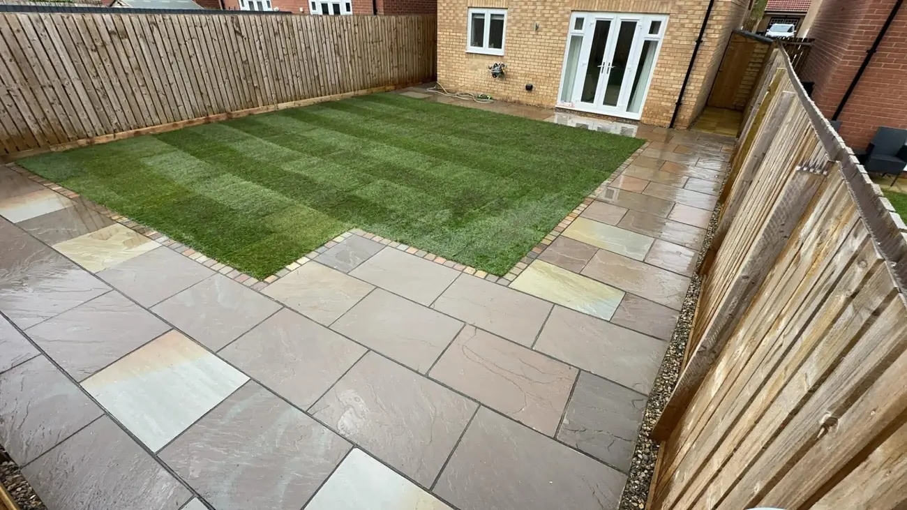 Indian stone patio around a turf lawn beside a timber fence