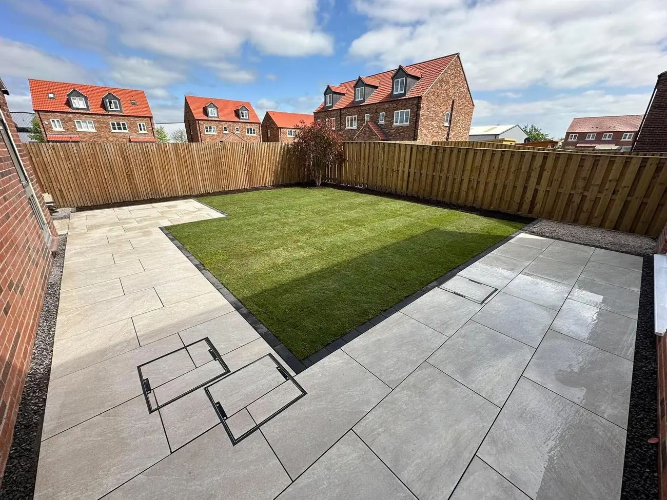 Porcelain patio wrapping around a new lawn with inspection covers set into the tiles