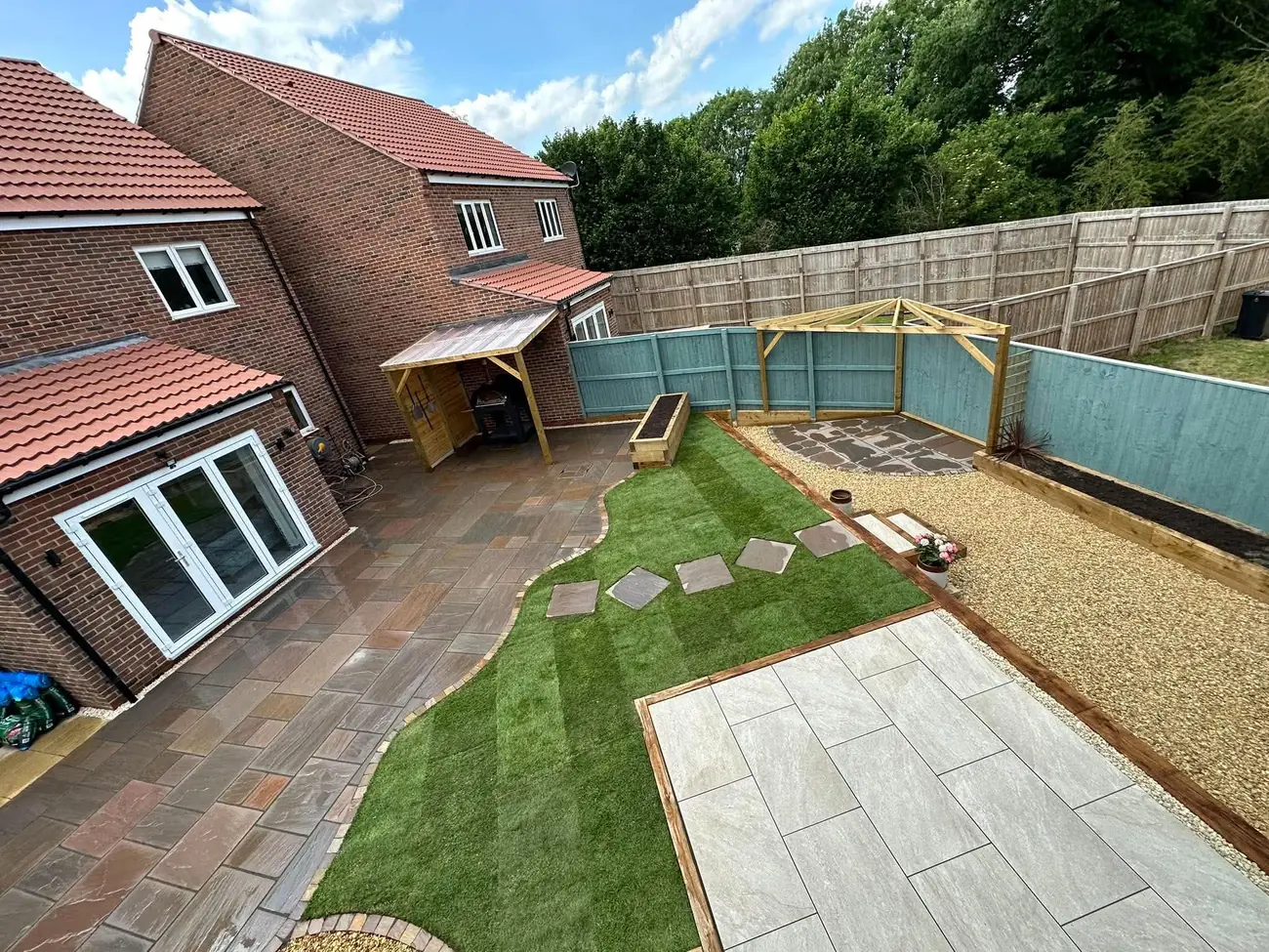 Aerial view of a full garden makeover with Indian stone paving, a curved lawn with stepping stones, gravel, sleeper beds and a porcelain patio
