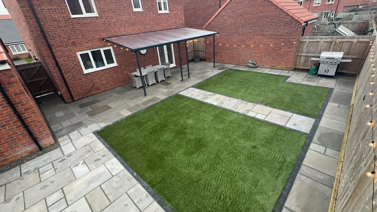 Grey Indian stone patio with two artificial grass panels, a covered dining area and a barbecue