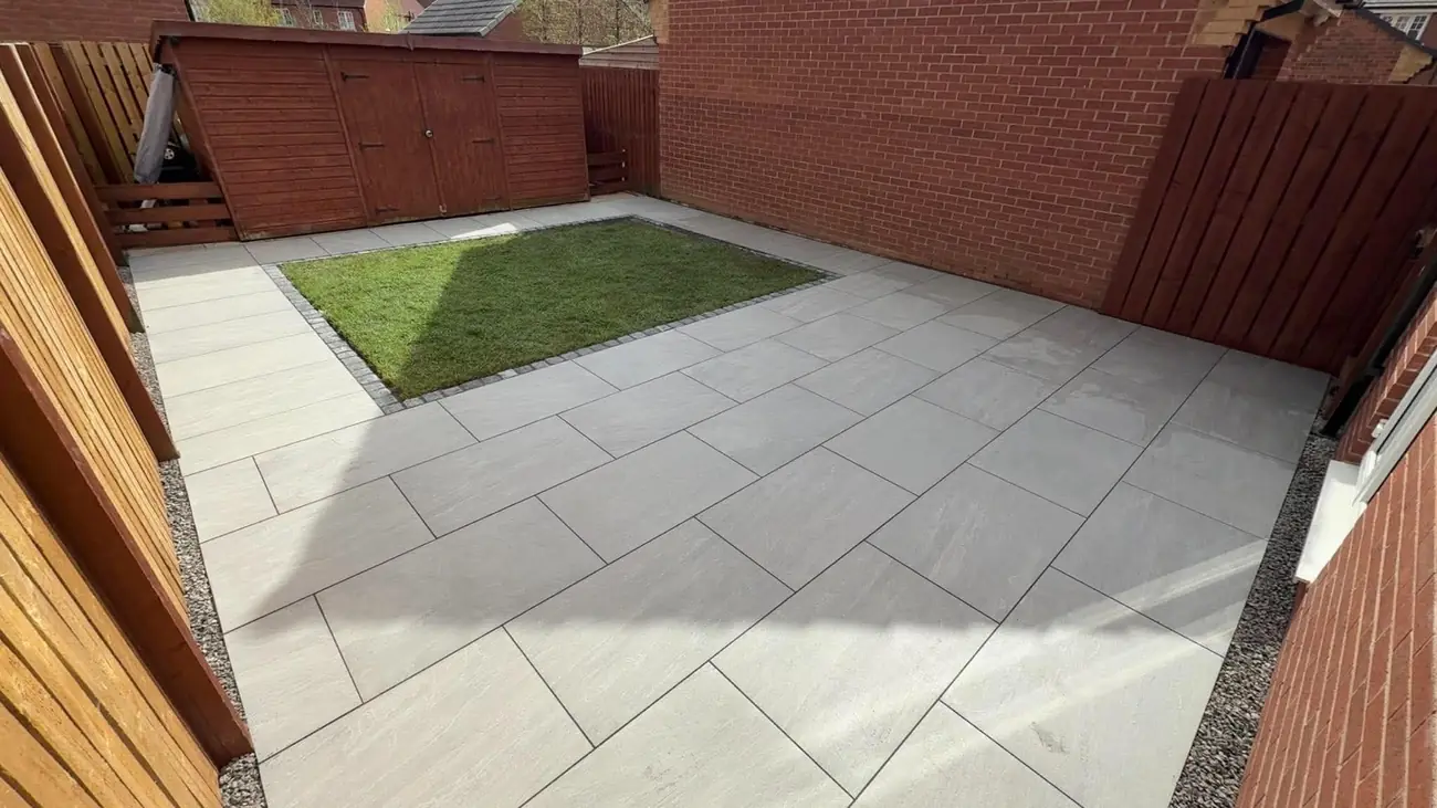 Porcelain patio with a lawn inset and block edging between red-stained fences
