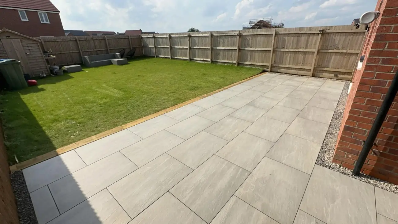 Large porcelain patio with a lawn edged in sleepers and new fencing