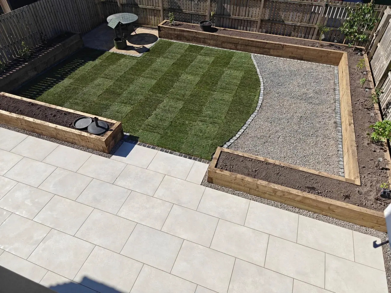 Aerial view of a porcelain patio beside a striped lawn, a gravel area and raised sleeper beds