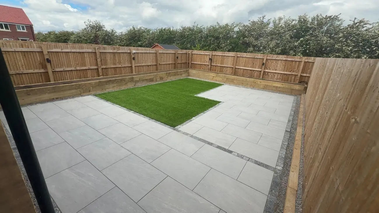 Grey porcelain patio with an artificial grass inset, block edging and sleeper beds