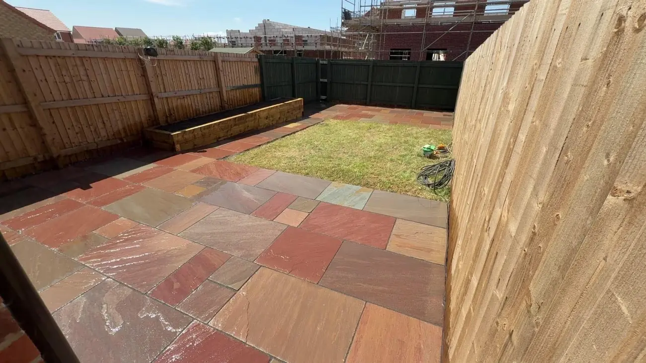 Red and buff Indian stone patio with a sleeper raised bed and lawn