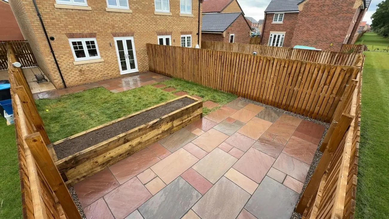 Indian stone patio with a sleeper raised bed, stepping stones and a lawn