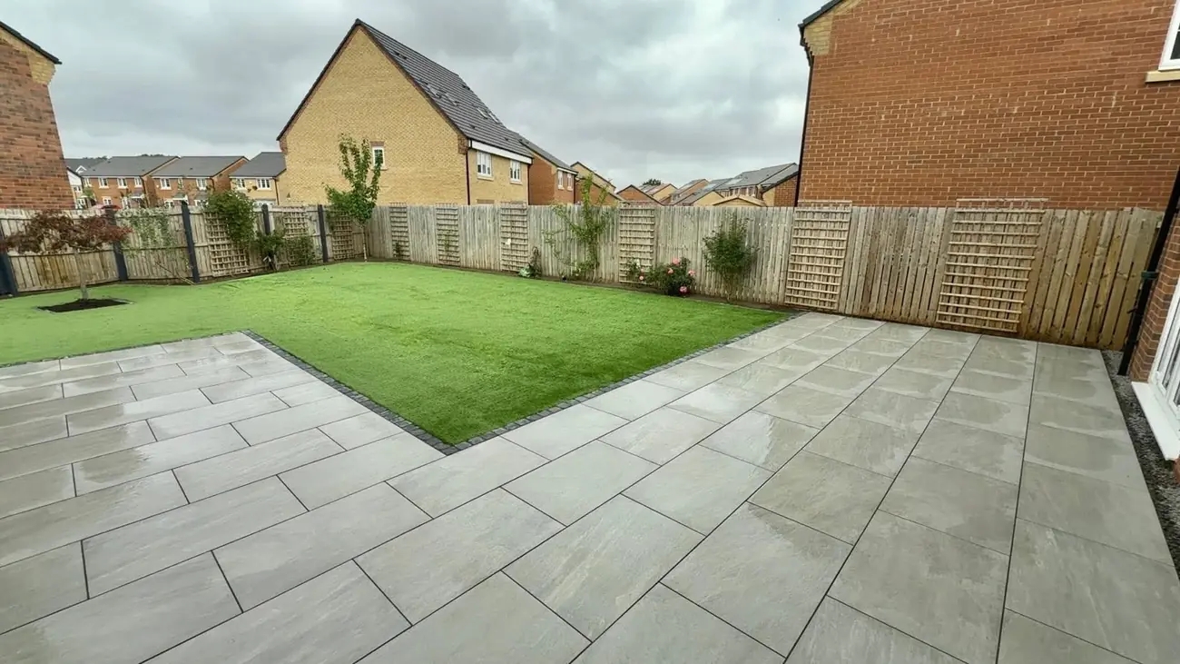 Grey porcelain patio beside an artificial grass lawn in a fenced garden