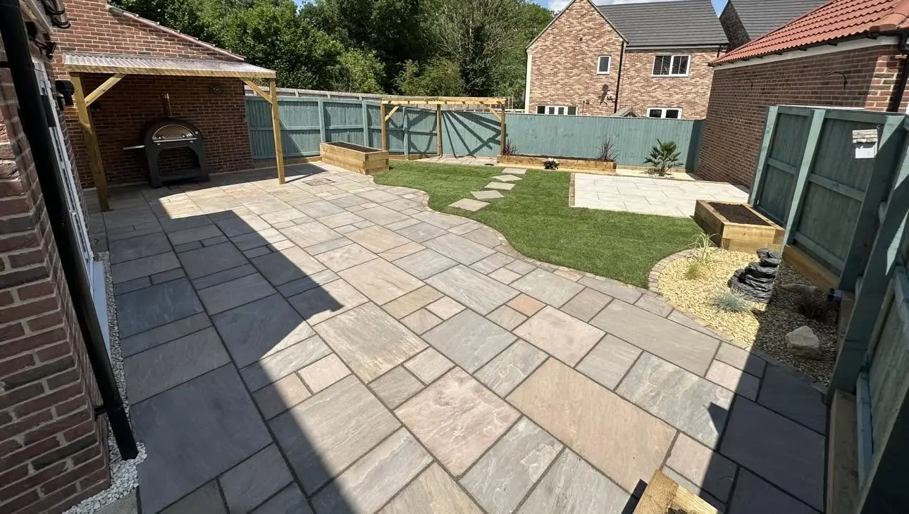 Large garden makeover with Indian stone and porcelain paving, a curved lawn, raised sleeper beds, a pergola and a covered outdoor cooking area