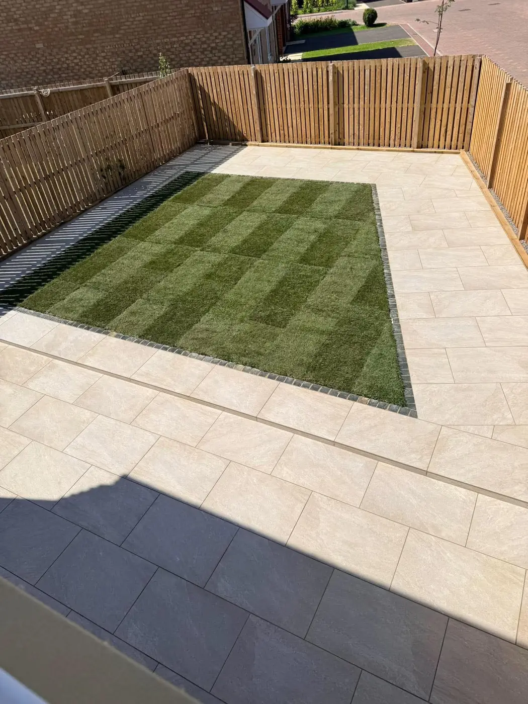 Cream porcelain patio around a striped turf lawn with block edging