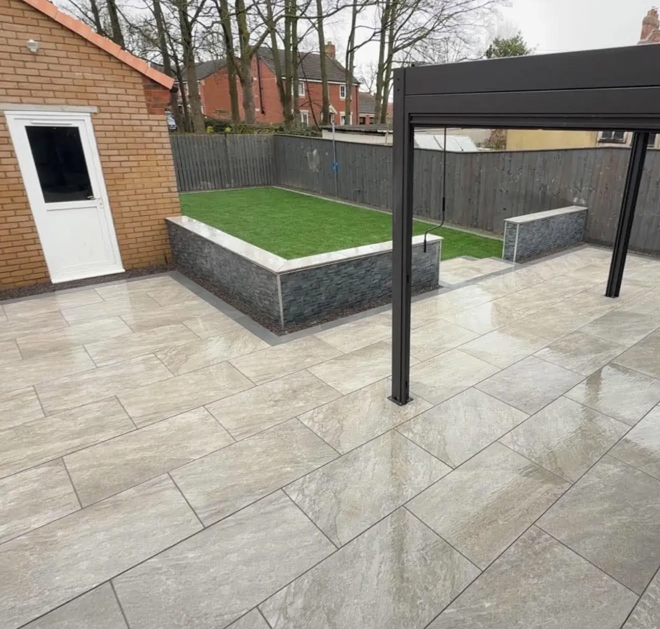 Stone-effect cladding on a raised lawn wall beside a porcelain patio with a pergola